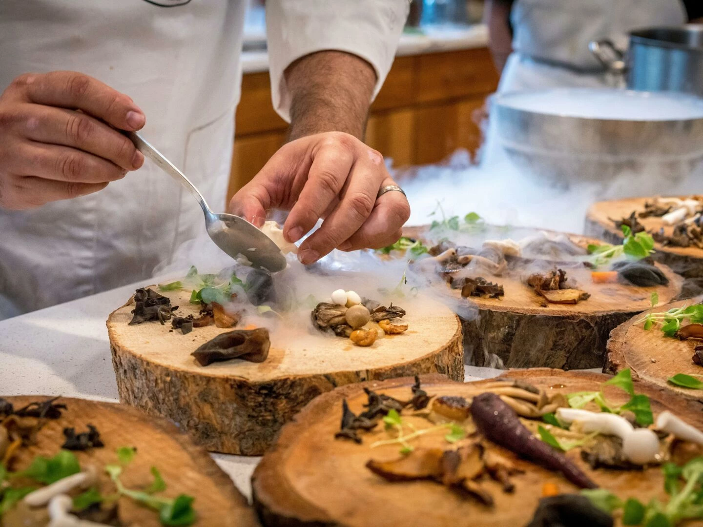 a chef artfully plating a gourmet dish with mushrooms and greens on wood slices