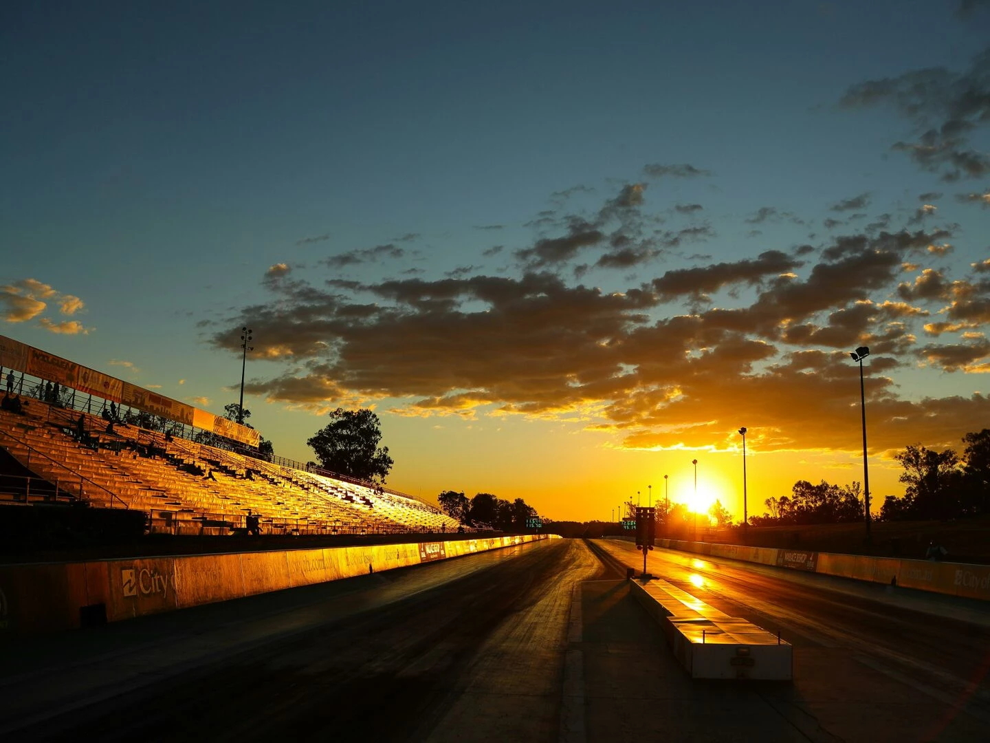 a stunning sunset illuminates an empty racetrack with bleachers highlighting the sky and track lines