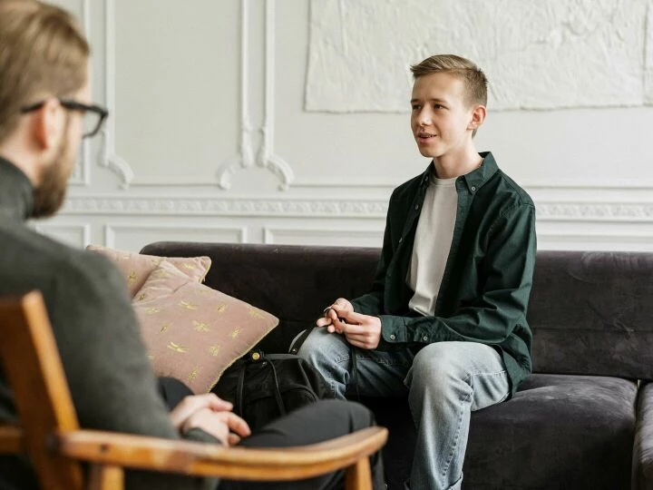 A teenage boy in a counseling session discussing with a therapist in an office setting.