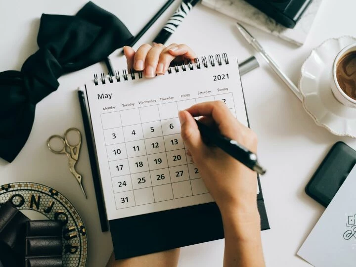 Top view of hands using a planner with coffee and accessories, focused on May 2021 calendar.