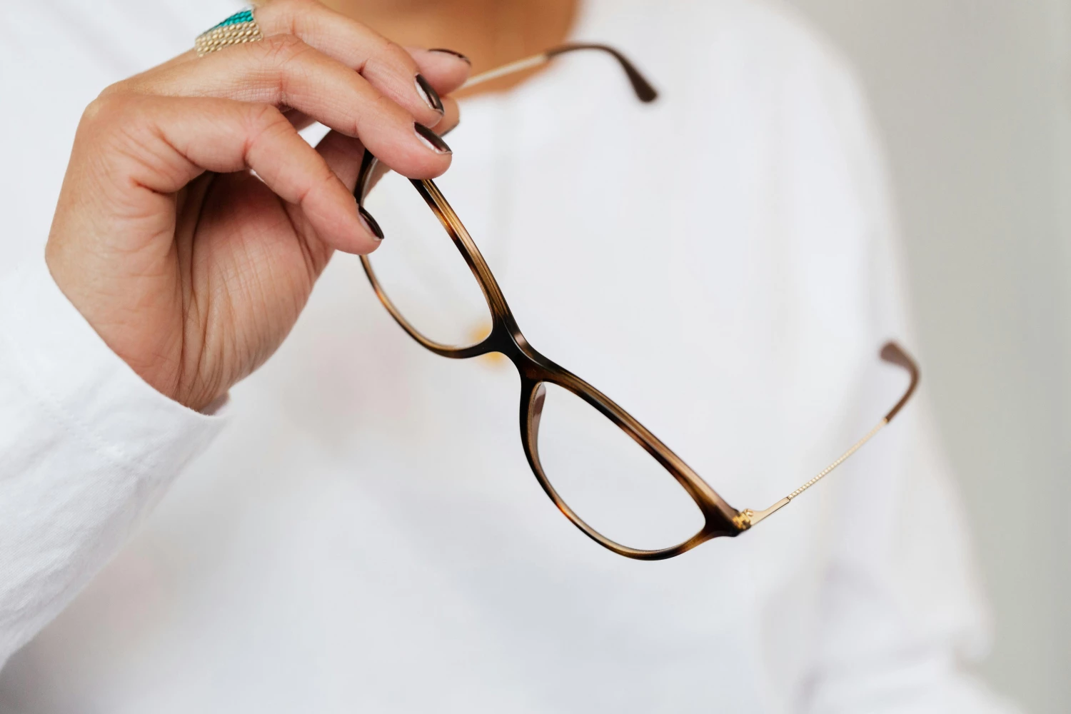 Crop unrecognizable elegant woman in white sweater and trendy optical glasses with brown frames and golden temples in hand