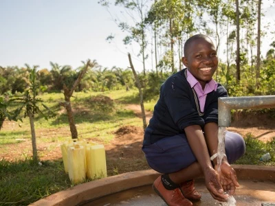 Prossy Nabiryo chair of St Balikddembe schools health club (SHC) using a new community water pump – Copyright All We Can