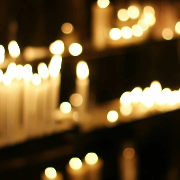 Close Up Photograph of Person Praying in Front Lined Candles