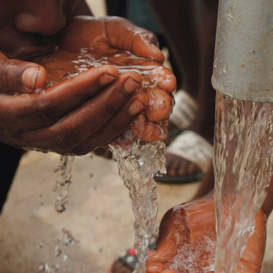 closeup of hands and face drinking fresh water from an outdoor tap emphasizing refreshment and necessity