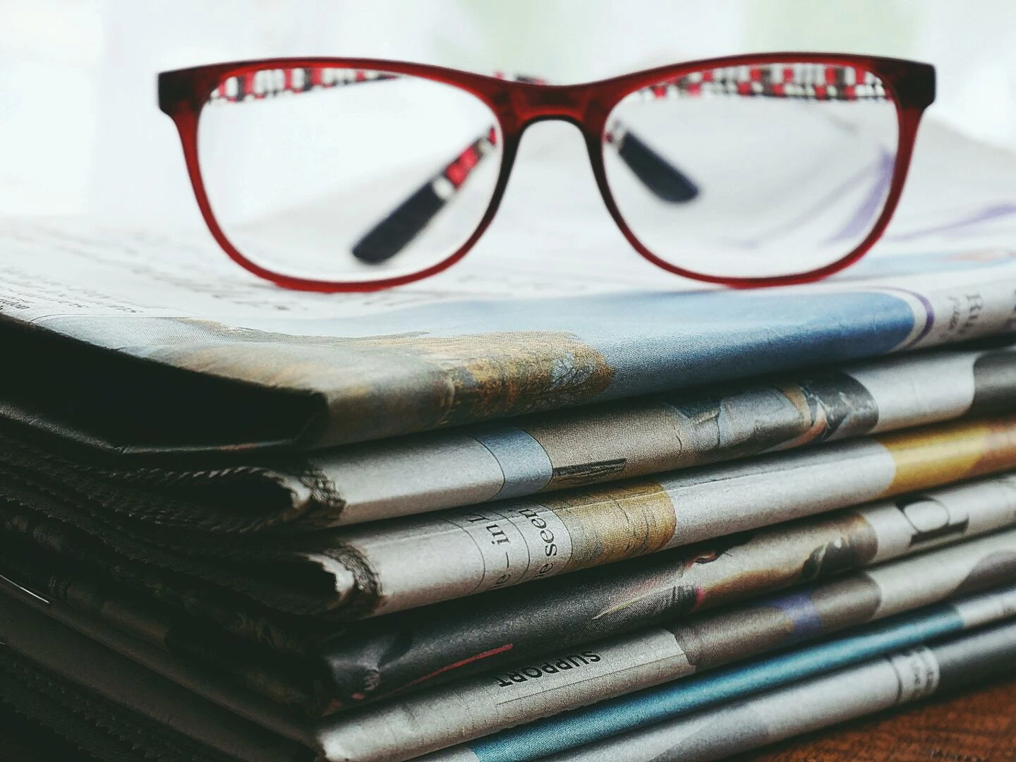 red eyeglasses resting on a stack of newspapers symbolize reading and information