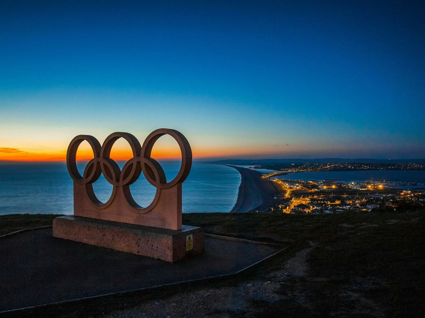 scenic sunset view of the olympic rings monument by the sea with city lights in the distance