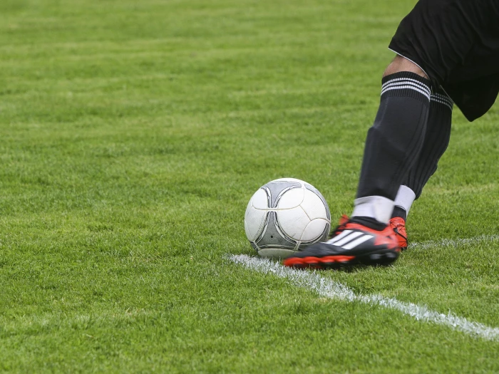 soccer player kicking white gray soccer ball on green grass field