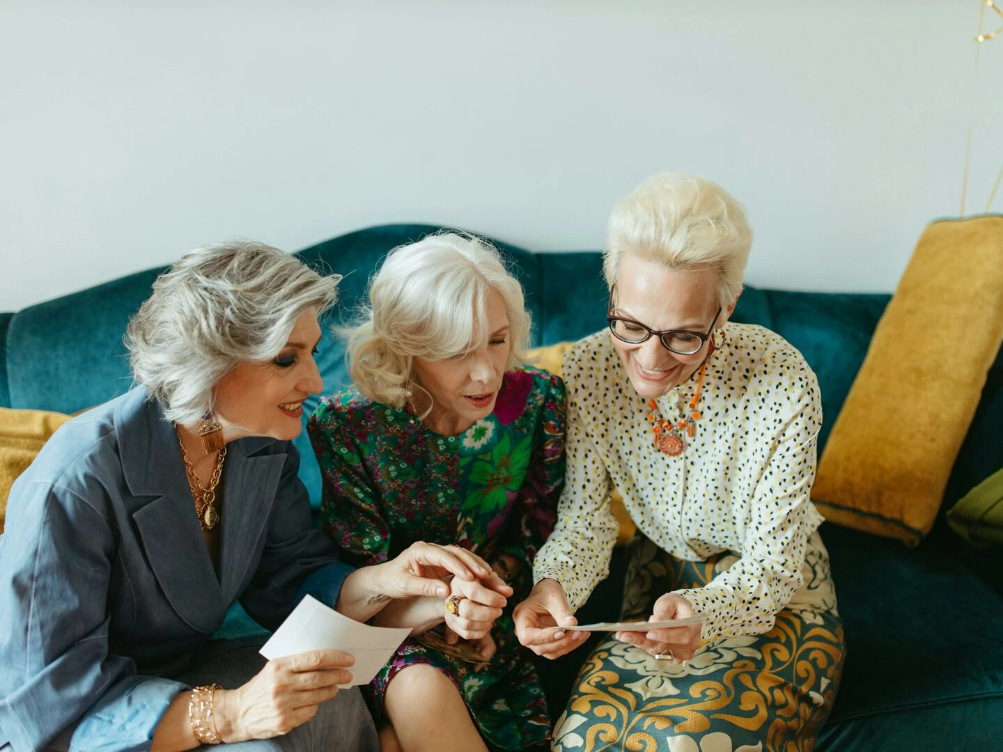 three senior women joyfully reminiscing over old photos on a cozy couch