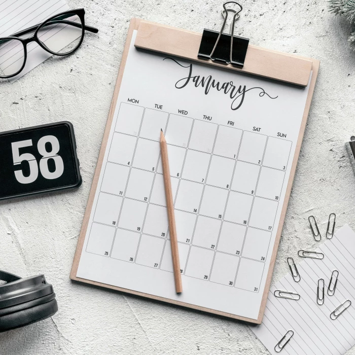 top view composition of clipboard with calendar and pencil placed on desk amidst stationery and eyeglasses